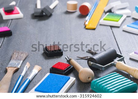 ink pads, plasticine blocks, brushes, paint roller and carving cutters on black wood table