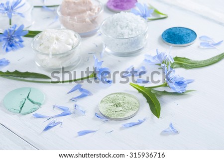 moisturizers, bath salts and powder compacts with blue chicory flowers on white wood table