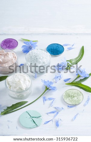 moisturizers, bath salts and powder compacts with blue chicory flowers on white wood table