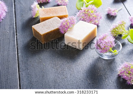 three different salt soaps and pink flowers on black wood background