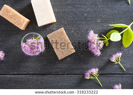 three different salt soaps and pink flowers on black wood background