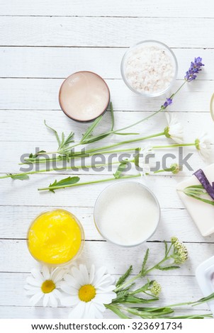 cosmetic creams, lip balm, soap  with herbal flowers on white wooden table