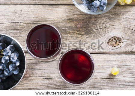 two glasses of red wine and grapes at bowls on old wooden table