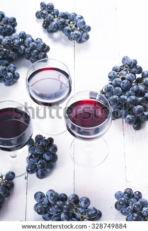 three glasses of red wine and blue grapes on white wooden table background