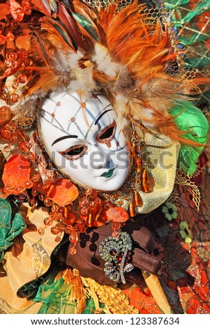 Vertical oriented image of white ornate mask with colorful feathers on traditional carnival costume in Venice, Italy.