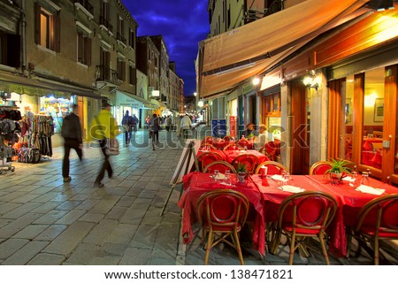 VENICE - NOV 13: Outdoor restaurant with red tables and chairs - one of the many bars and restaurants popular with tourists in the evening hours on streets of Venice, Italy on November 13, 2012.