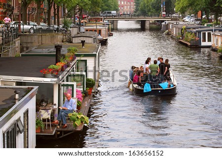 AMSTERDAM - JULY 15: Boat with tourists passing by houseboats on city canal. Houseboats are high demand very popular and common form of housing in Amsterdam, Netherlands on July 15, 2007.
