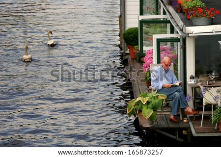 AMSTERDAM - JULY 15: Two white swans passing by houseboat on city canal. Houseboats are high demand very popular and common form of housing in Amsterdam, Netherlands on July 15, 2007.