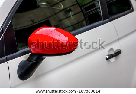 Water drops on red side mirror of white car.