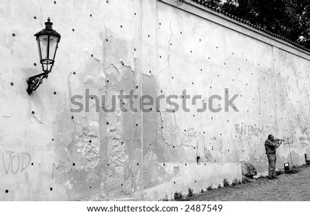 Unidentified street musician standing near the wall and playing on violin in Prague, Czech Republic (monochrome).