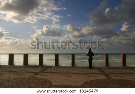 Unidentified person standing on promenade and watching on the sea under the beautiful sky in Tel Aviv, Israel.