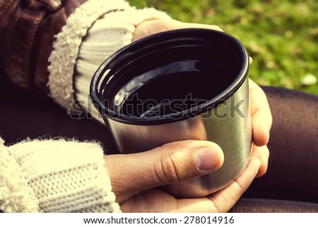 Hands holding thermos cup of tea isolated outdoors