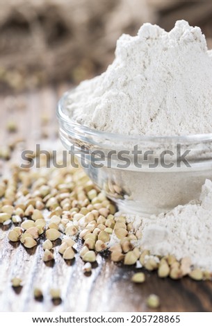 Heap of Buckwheat Flour (close-up shot) with some grains on wooden background
