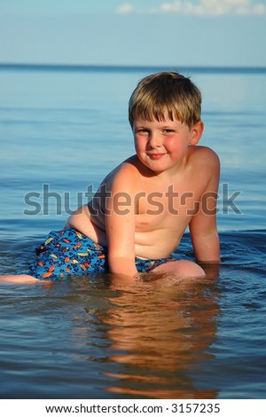 A happy boy poses in calm blue water, late evening light.