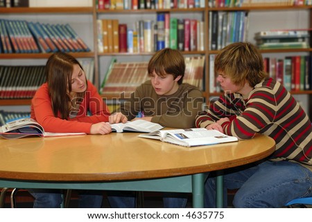 Three teen high school students work together studying in school library.
