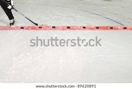 Young Hockey Player Practices Shooting Pucks with stick in Hockey Rink
