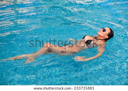Sexy swimmer. A slender sexy lady in bikini balancing on her back in blue water.