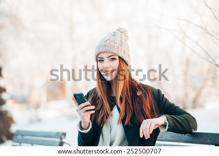 young woman in winter park talking mobile phone, sms, sitting on the bench