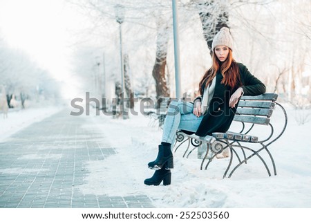 young woman in winter park sitting on the bench