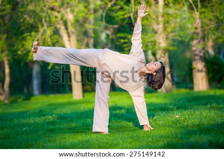 Yoga utthita trikonasana triangle pose by woman in white costume on green grass in the park around pine trees