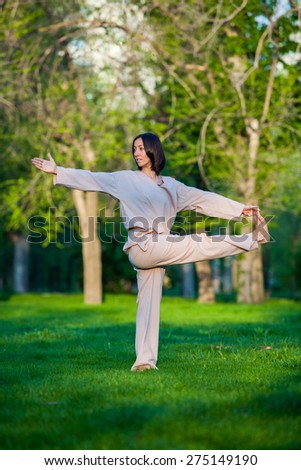 Yoga utthita trikonasana triangle pose by woman in white costume on green grass in the park around pine trees