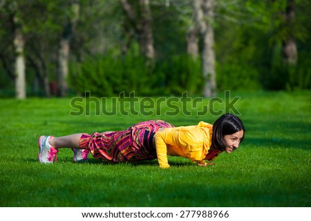 Push ups or press ups exercise by young woman. Girl working out on grass crossfit strength training in the glow of the morning sun