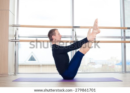 Side view of a fit young man doing the cobra pose in a bright fitness studio