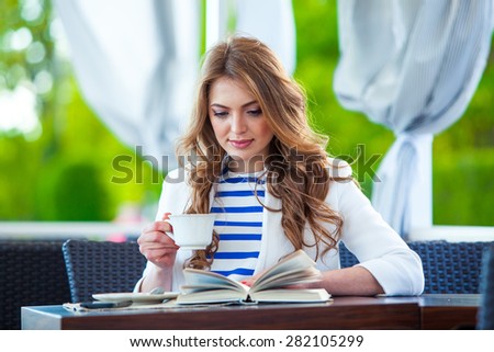 beautiful young girl in outdoor cafe reading a book and drinking coffee. phone. student. business woman