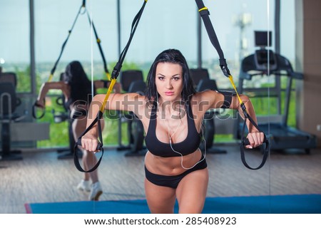 attractive woman does crossfit push ups with trx fitness straps in the gym\'s studio