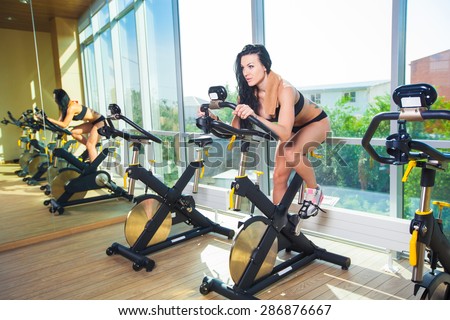 Beautiful woman at the gym on bike, cycle, sunny gym, general plan