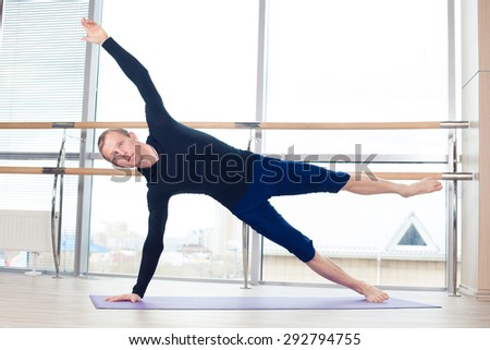 Side view of a fit young man doing the cobra pose in a bright fitness studio