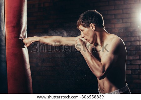 muscular handsome fighter giving a forceful forward kick during a practise round with a boxing bag, kickboxing.