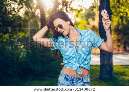 young beautiful short blue hair hipster woman with headphones music in the park. ice cream.