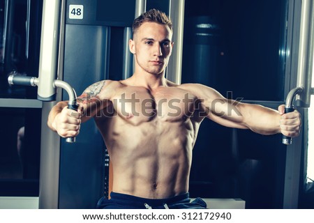 Brutal athletic man pumping up muscles on crossover.