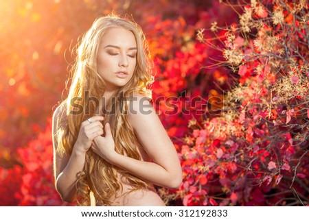 young woman on a background of red and yellow autumn leaves with beautiful curly hair on his chest, with no clothes