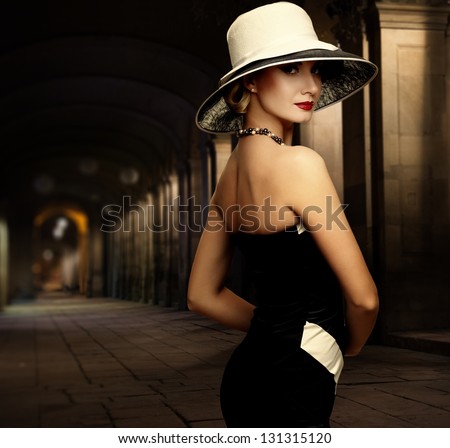 Woman in black dress and big white hat alone outdoors at night