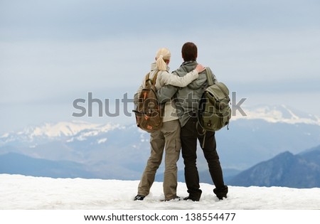 Couple of hikers with backpacks looking over mountains view