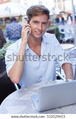 Handsome young man with laptop and mobile phone calling in a summer cafe