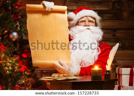Santa Claus in wooden home interior holding blank wish list scroll