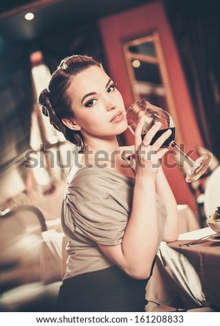 Beautiful young girl with glass of red wine alone in a restaurant