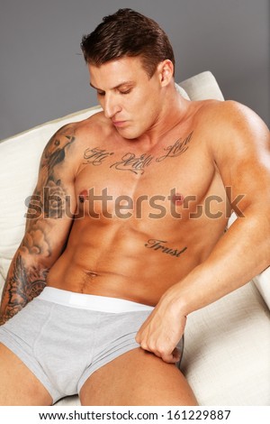 Man with beautiful muscular tattooed torso in underwear lying on sofa