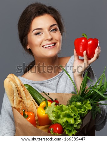 Smiling young brunette woman with grocery bag full of fresh vegetables