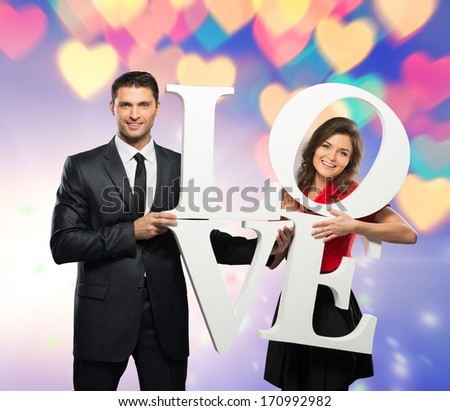 Beautiful smiling couple holding word LOVE over bokeh background