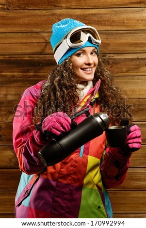 Happy woman in ski wear with thermos against wooden wall