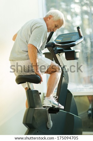 Senior man adjusting seat on a bike machine in a fitness club