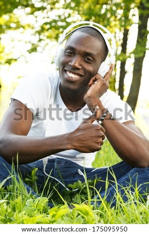 Positive young african american man in white shirt listens music in a park