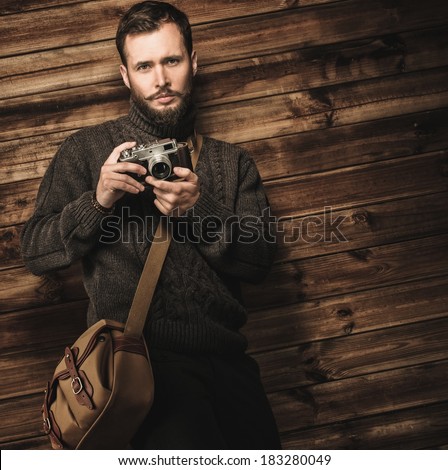 Handsome man wearing cardigan with vintage camera in wooden house interior