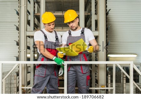 Two workers in safety hats on a factory reading plan