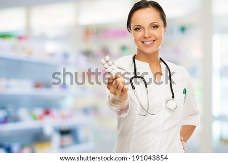 Young positive brunette doctor woman holding pills in drug store