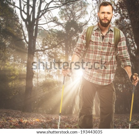 Handsome traveler with backpack and hiking poles in autumnal forest